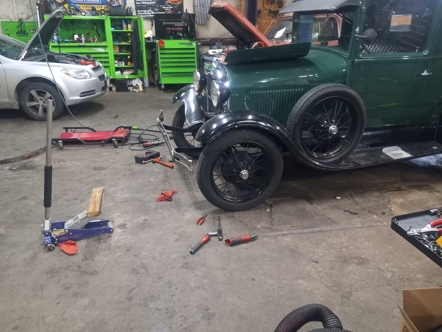 A green Ford Model A pickup and a modern sedan being serviced side by side in the shop