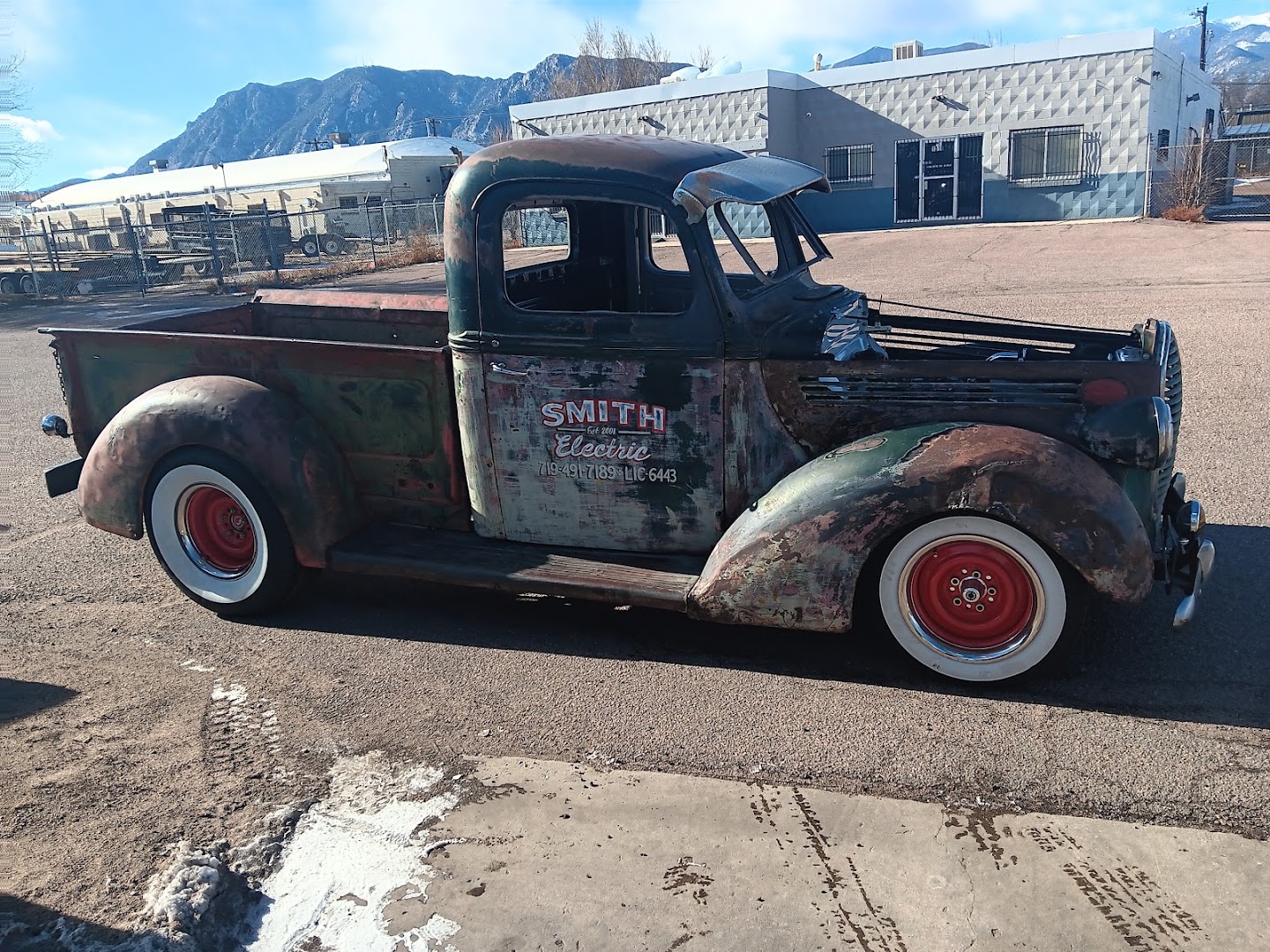 A patina shop truck parked outside with Cheyenne Mountain behind it