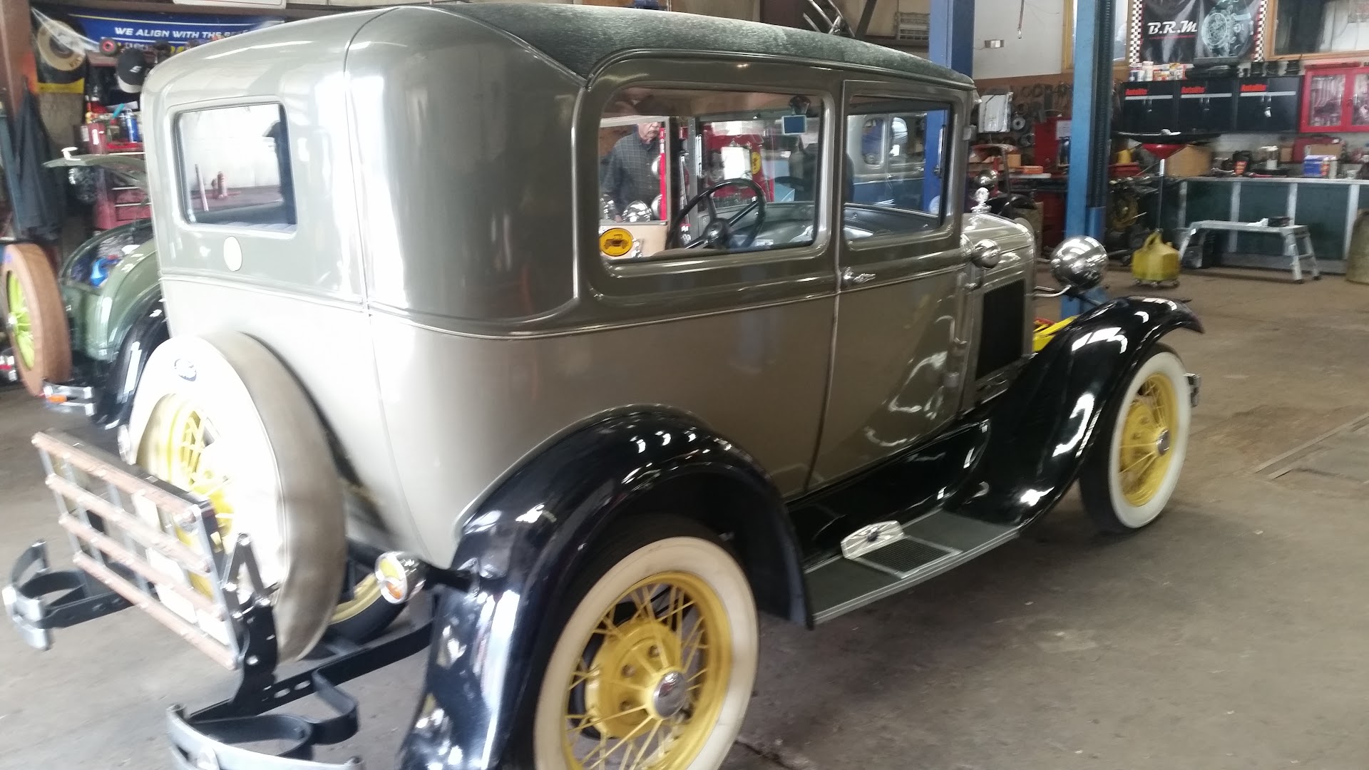 A tan and green Ford Model A sedan inside the shop