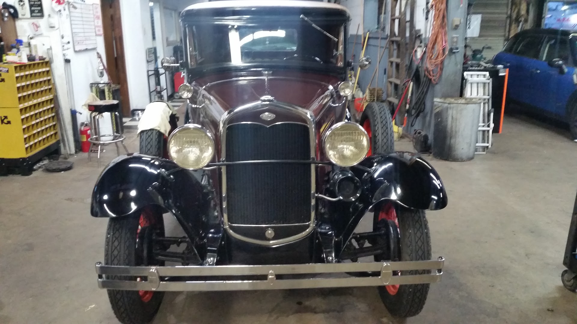 A maroon and black Ford Model A facing the camera in the shop