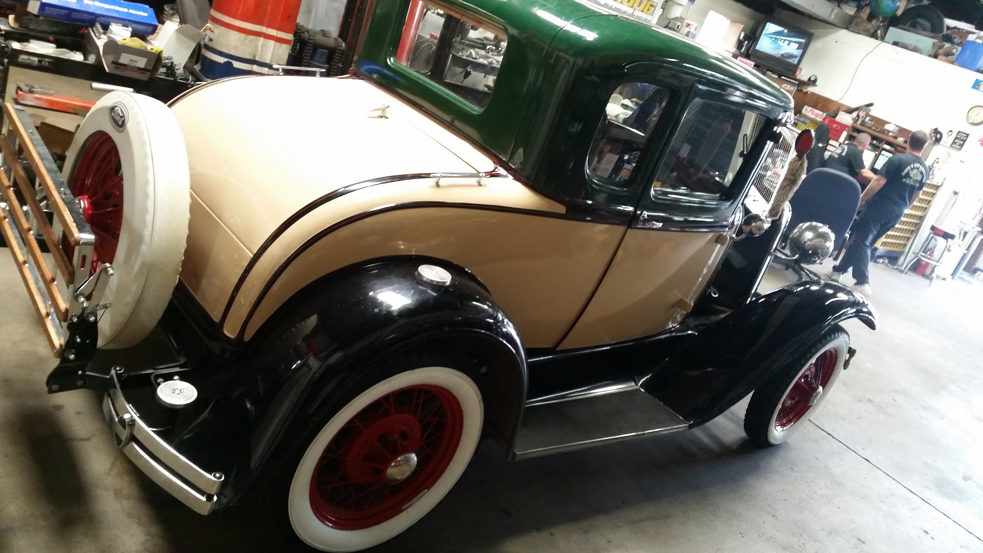 A green and tan Ford Model A coupe with red wheels in the shop